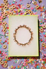 Bracelet on a white card with colorful cereal and sprinkles on a purple background