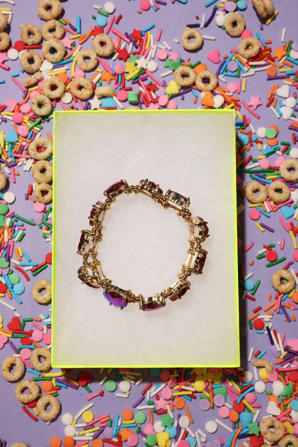 Gold bracelet on a white card with colorful cereal and sprinkles in the background