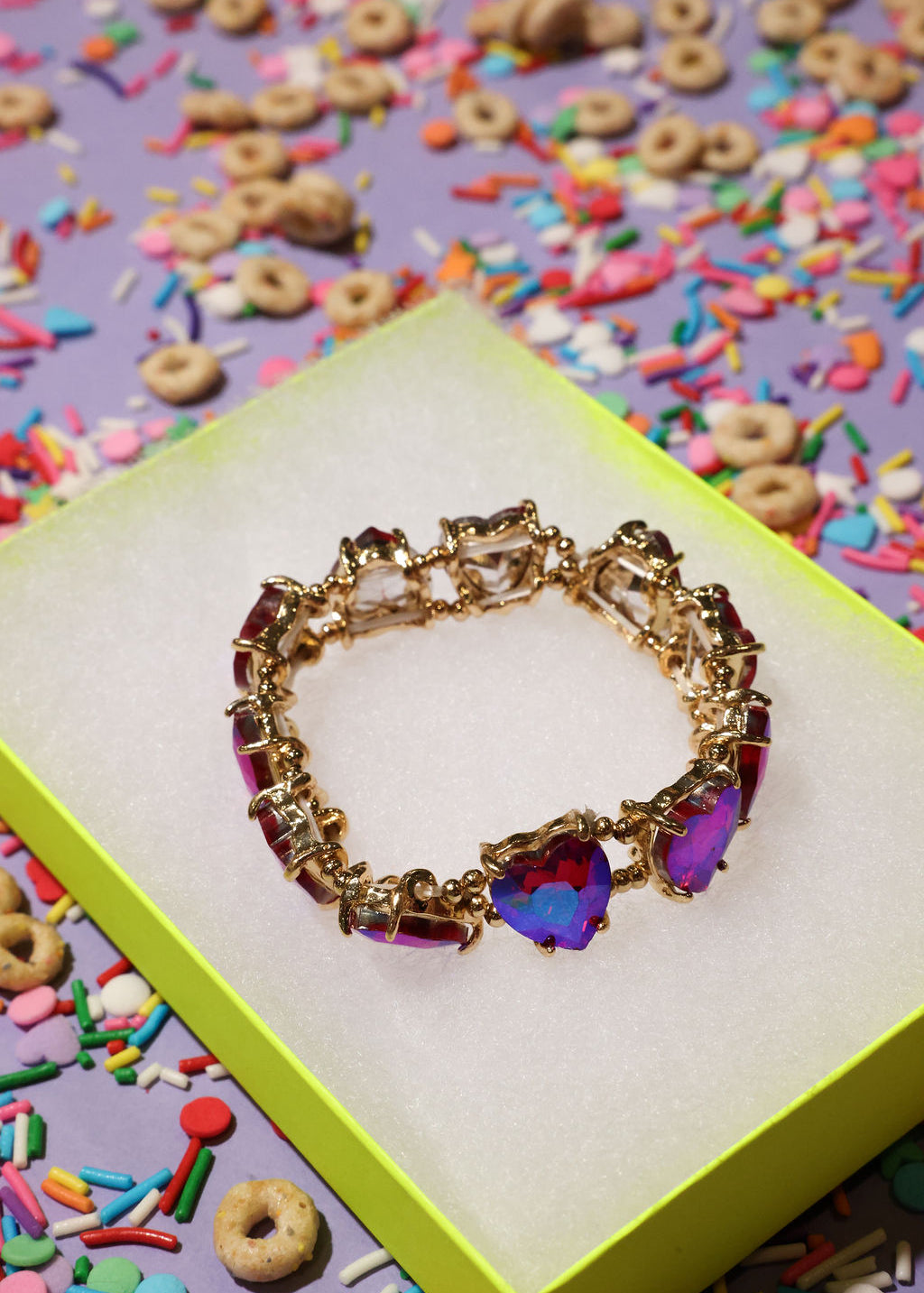 Gold bracelet with colorful heart-shaped stones on a box with cereal and sprinkles in the background