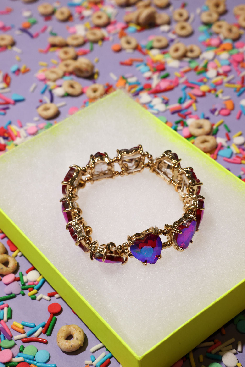 Gold bracelet with colorful heart-shaped stones on a box with cereal and sprinkles in the background