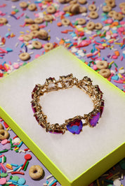Gold bracelet with colorful heart-shaped stones on a box with cereal and sprinkles in the background