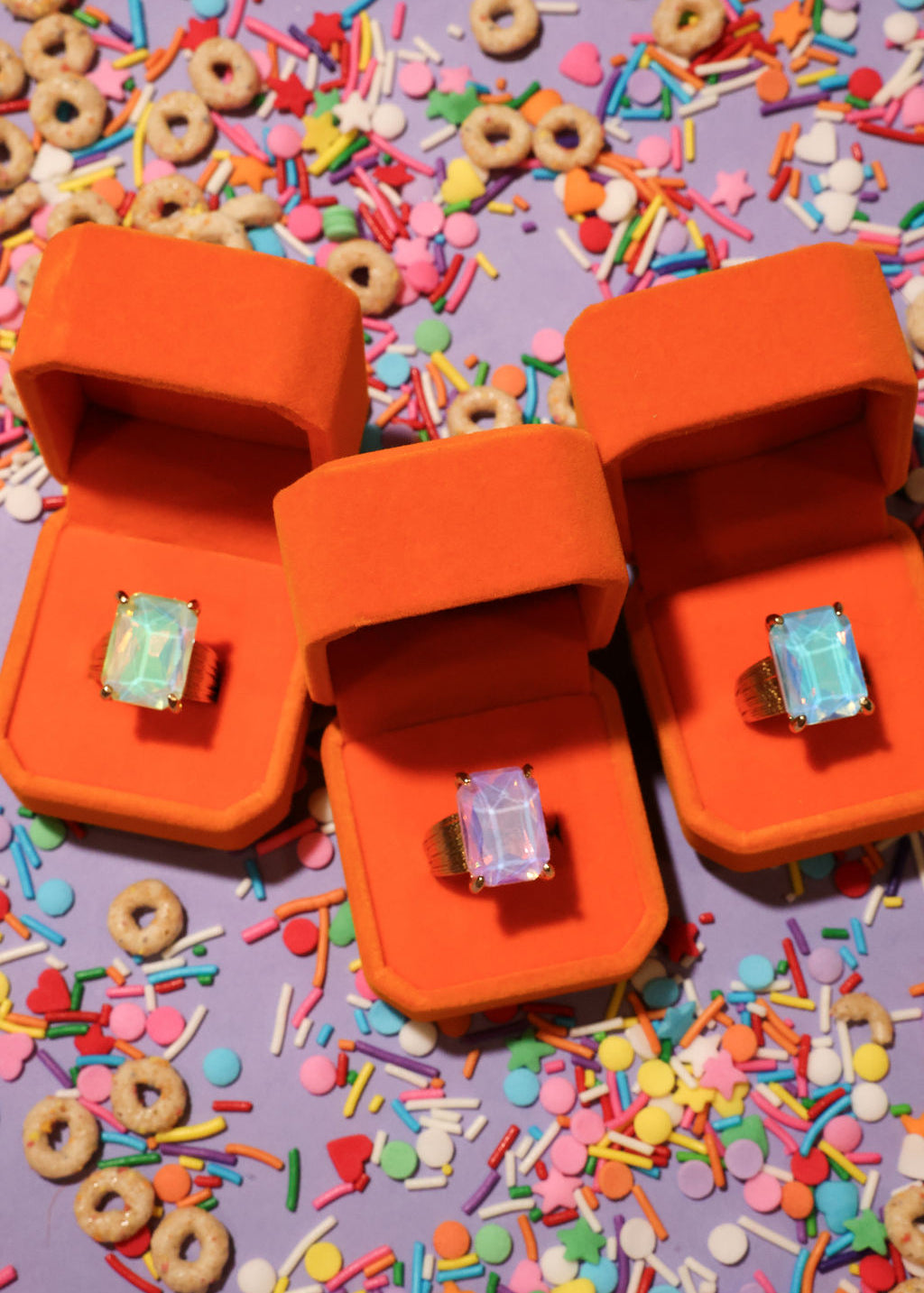 Two orange jewelry boxes with rings on a colorful sprinkles background