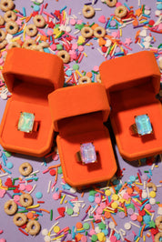 Two orange jewelry boxes with rings on a colorful sprinkles background