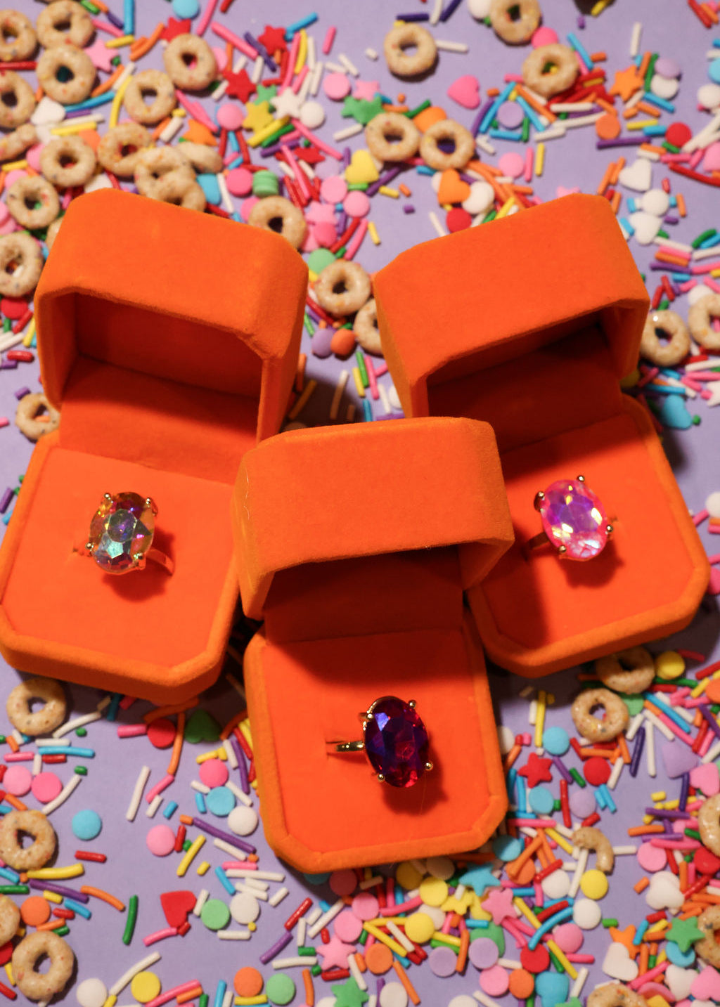 Three orange jewelry boxes with rings on a colorful sprinkles background