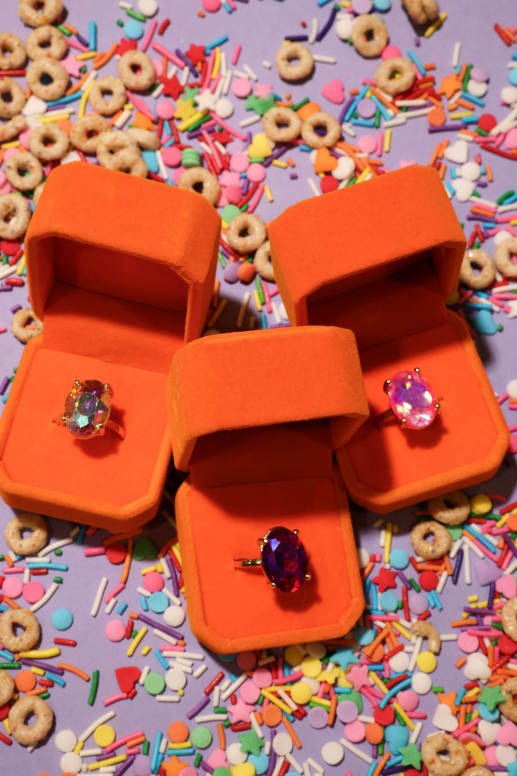 Three orange jewelry boxes with rings on a colorful sprinkles background