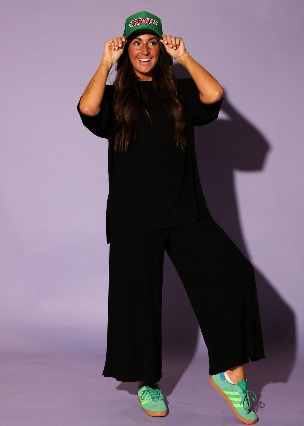 Front view of a model wearing a black ribbed two piece set, including a loose fitting, short sleeve top and high waisted pants. The model is standing with a relaxed posture and wearing green sneakers