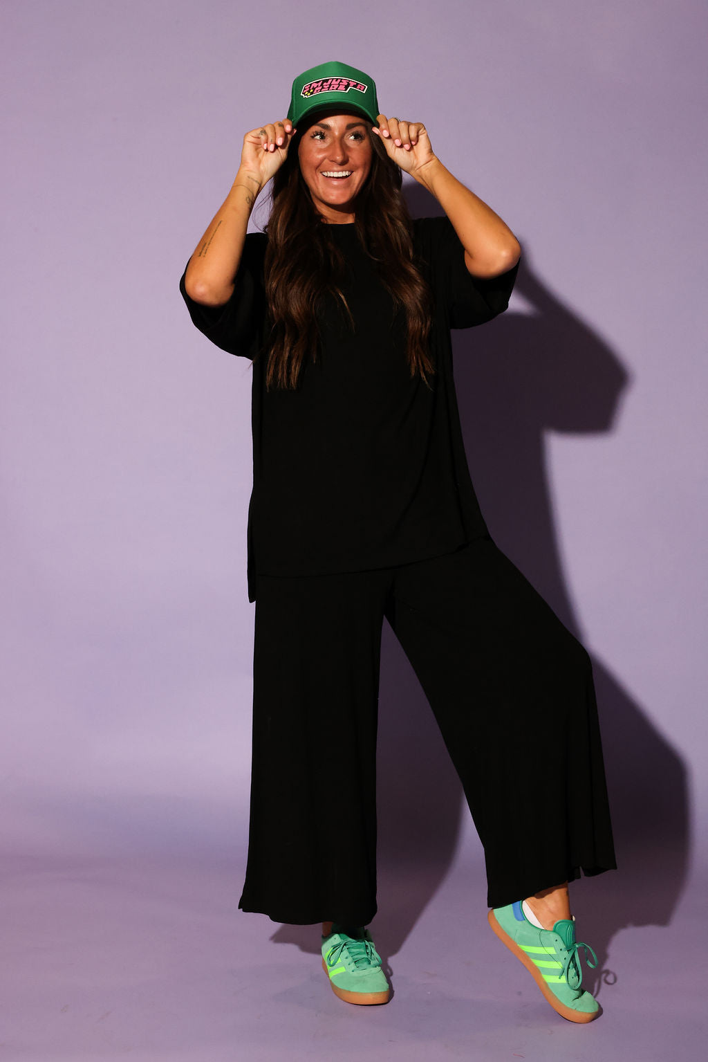 Front view of a model wearing a black ribbed two piece set, including a loose fitting, short sleeve top and high waisted pants. The model is standing with a relaxed posture and wearing green sneakers