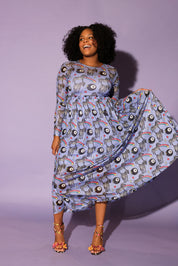 Model wearing a black trucker hat with red and yellow circle logo, long purple mesh dress with a zebra, rainbow and 8 ball design print, in front of a purple background, full frontal view