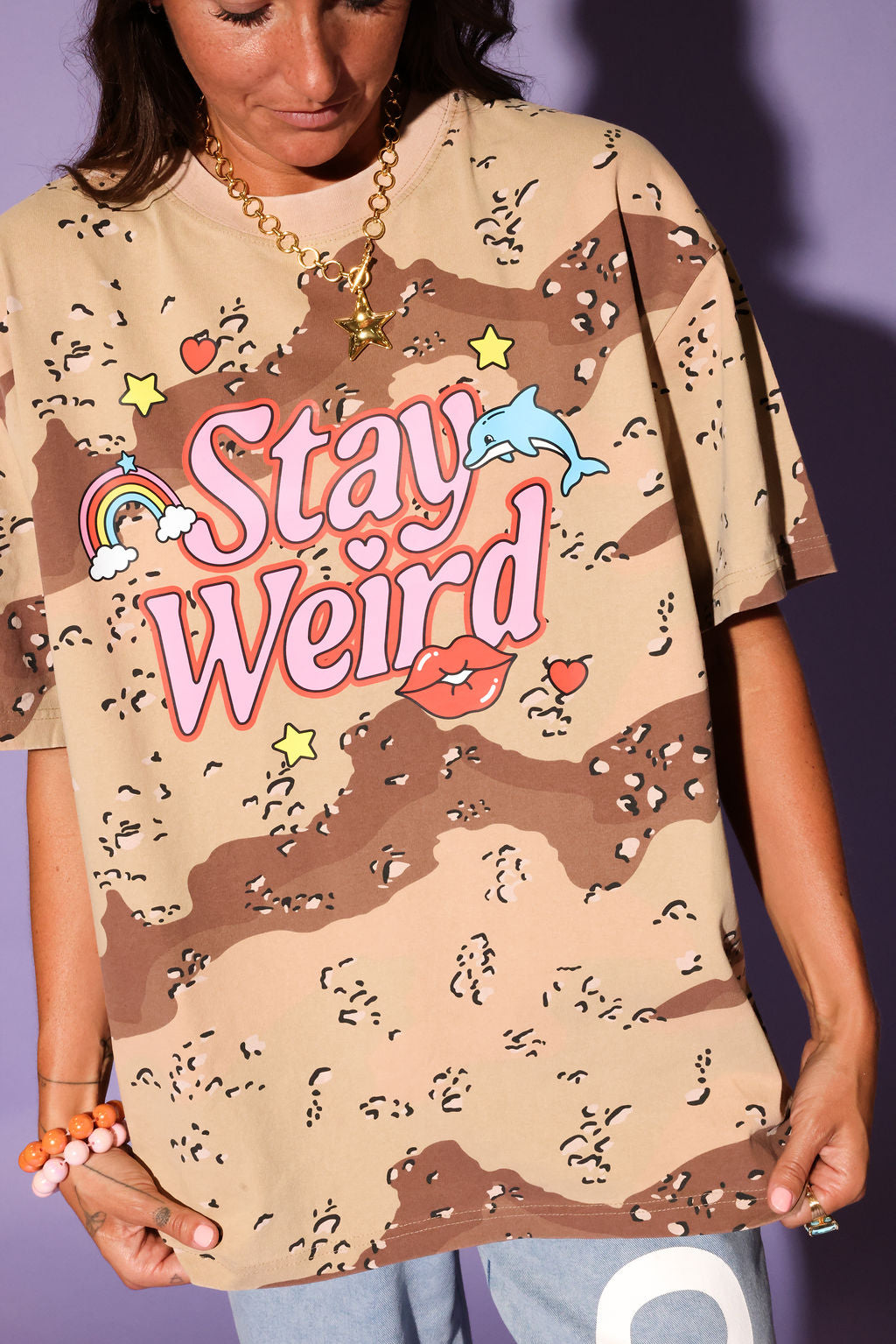 Person wearing a camouflage t-shirt with 'Stay Weird' text and graphics, close up view