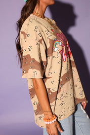 Person wearing a camouflage shirt with 'Stay Weird' text, light blue pants against a purple background, side view