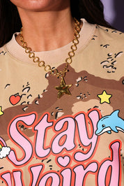 Person wearing a gold chain necklace with a star pendant, standing in front of a graphic design with text and graphics