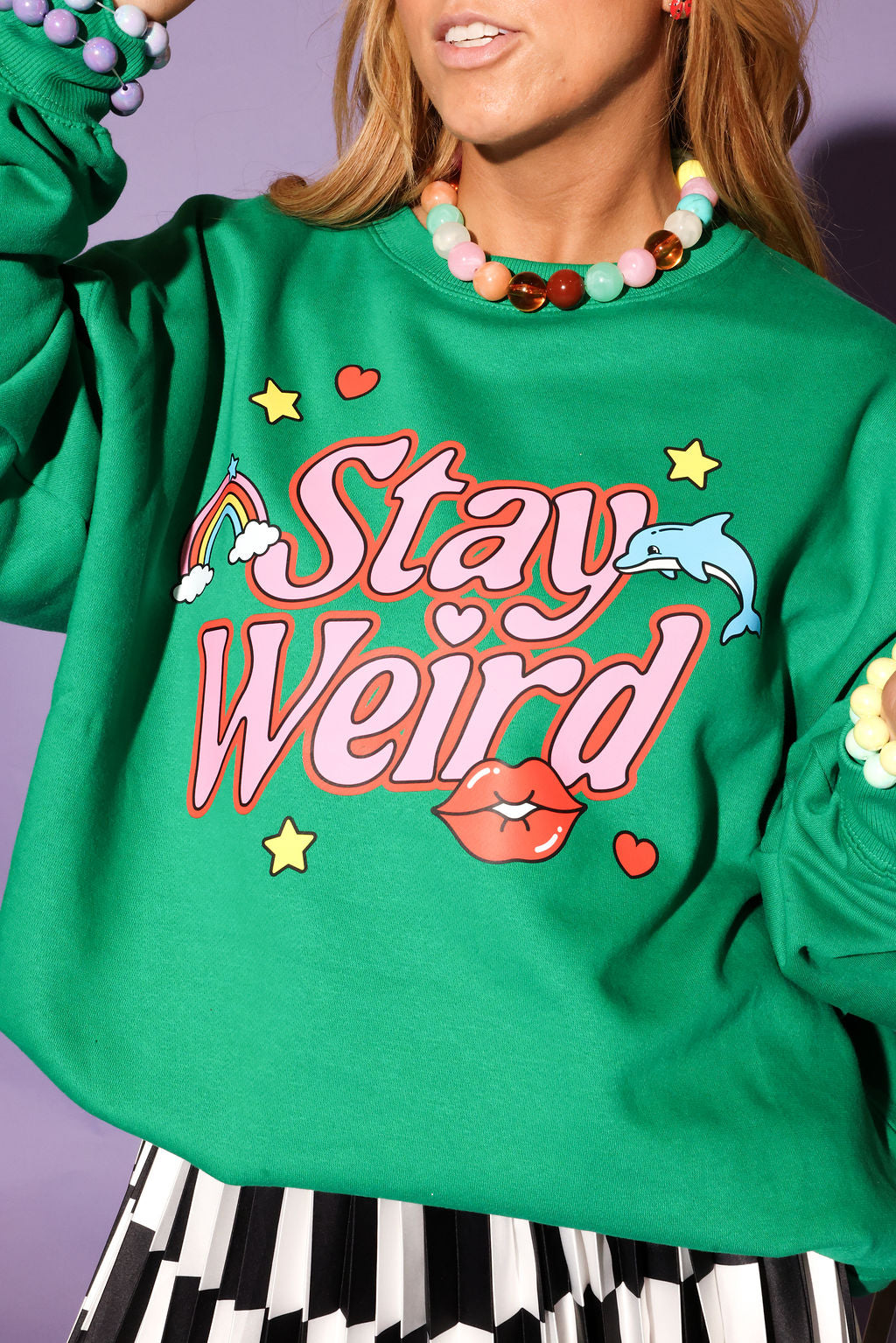 Green sweatshirt with 'Stay Weird' text and colorful graphics on a purple background, close up frontal view