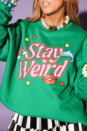 Green sweatshirt with 'Stay Weird' text and colorful graphics on a purple background, close up frontal view
