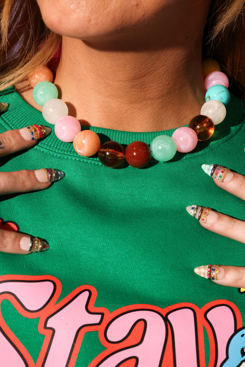 Close-up of a colorful beaded necklace on a person wearing a green shirt with pink text