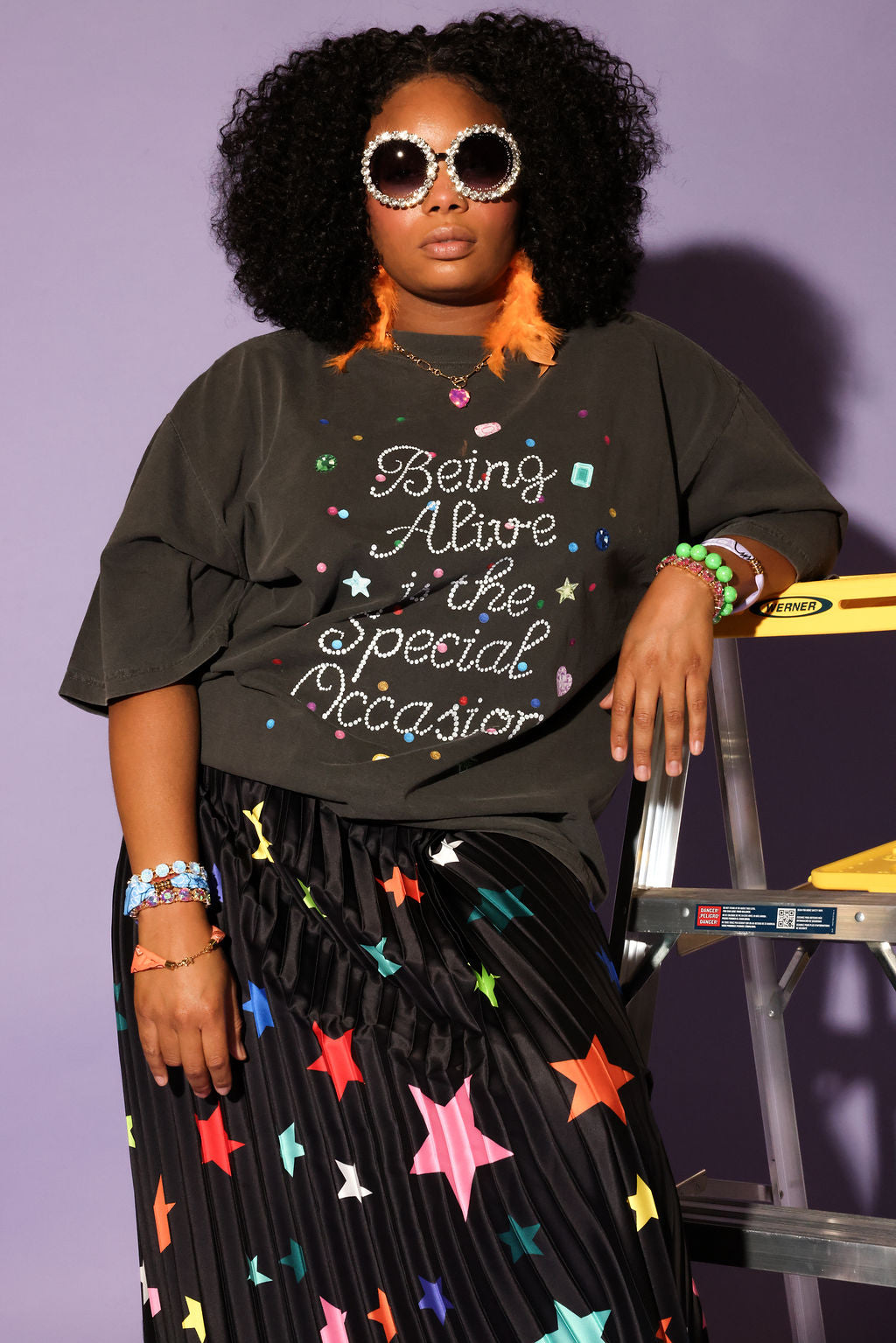 Woman wearing a grey t-shirt with colorful text and a star-patterned skirt against a purple background, frontal view