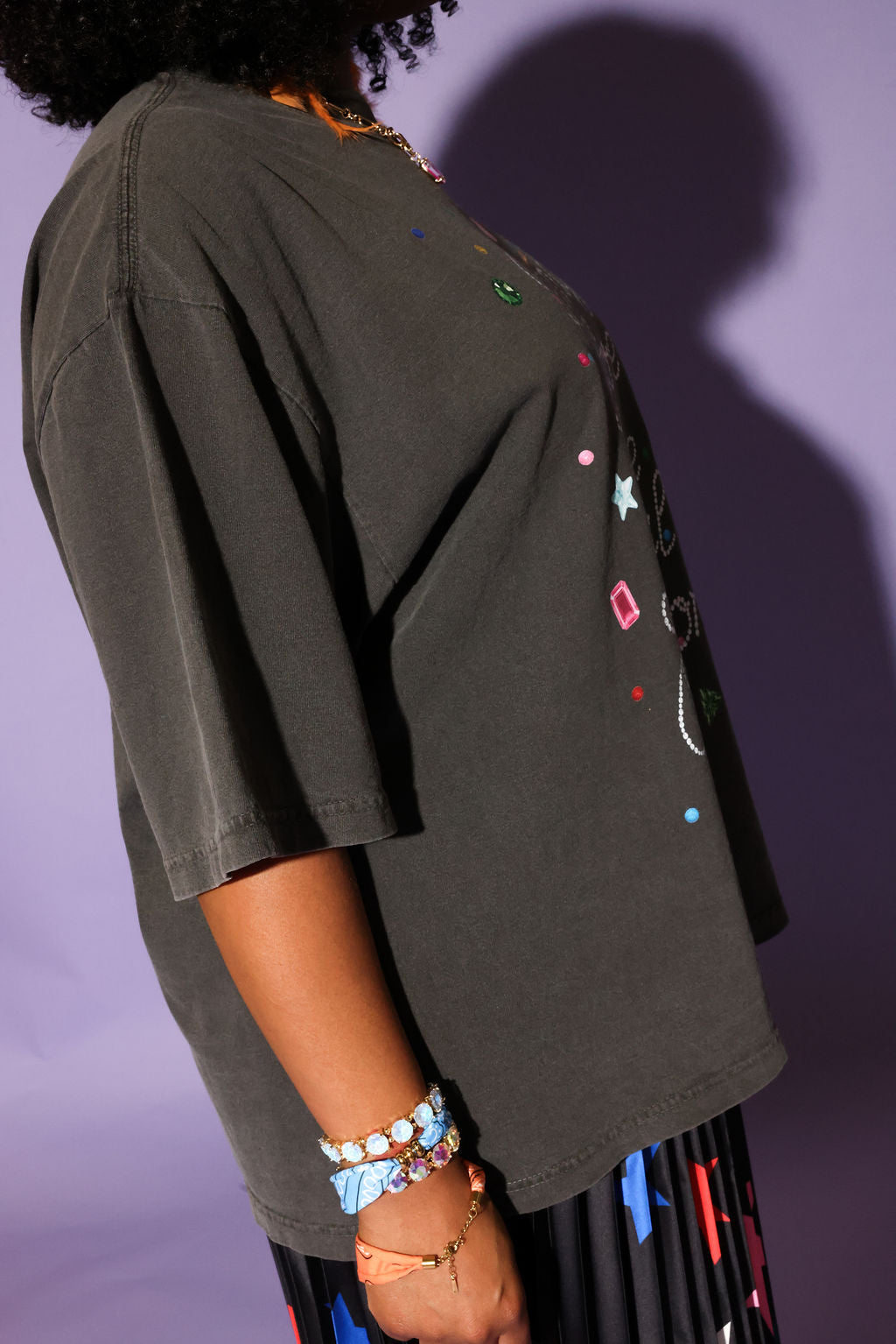 Woman wearing a gray graphic t-shirt and star-patterned skirt against a purple background, side view