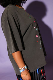 Woman wearing a gray graphic t-shirt and star-patterned skirt against a purple background, side view