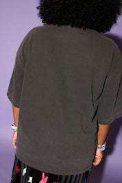 Person wearing a dark gray oversized t-shirt against a purple background, back view