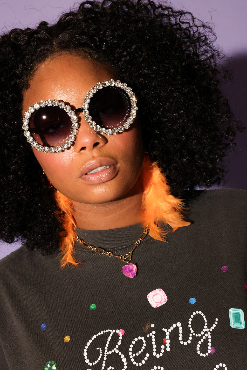Model wearing large, round sunglasses with a black shirt featuring colorful text and designs, frontal view