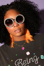Model wearing large, round sunglasses with a black shirt featuring colorful text and designs, frontal view