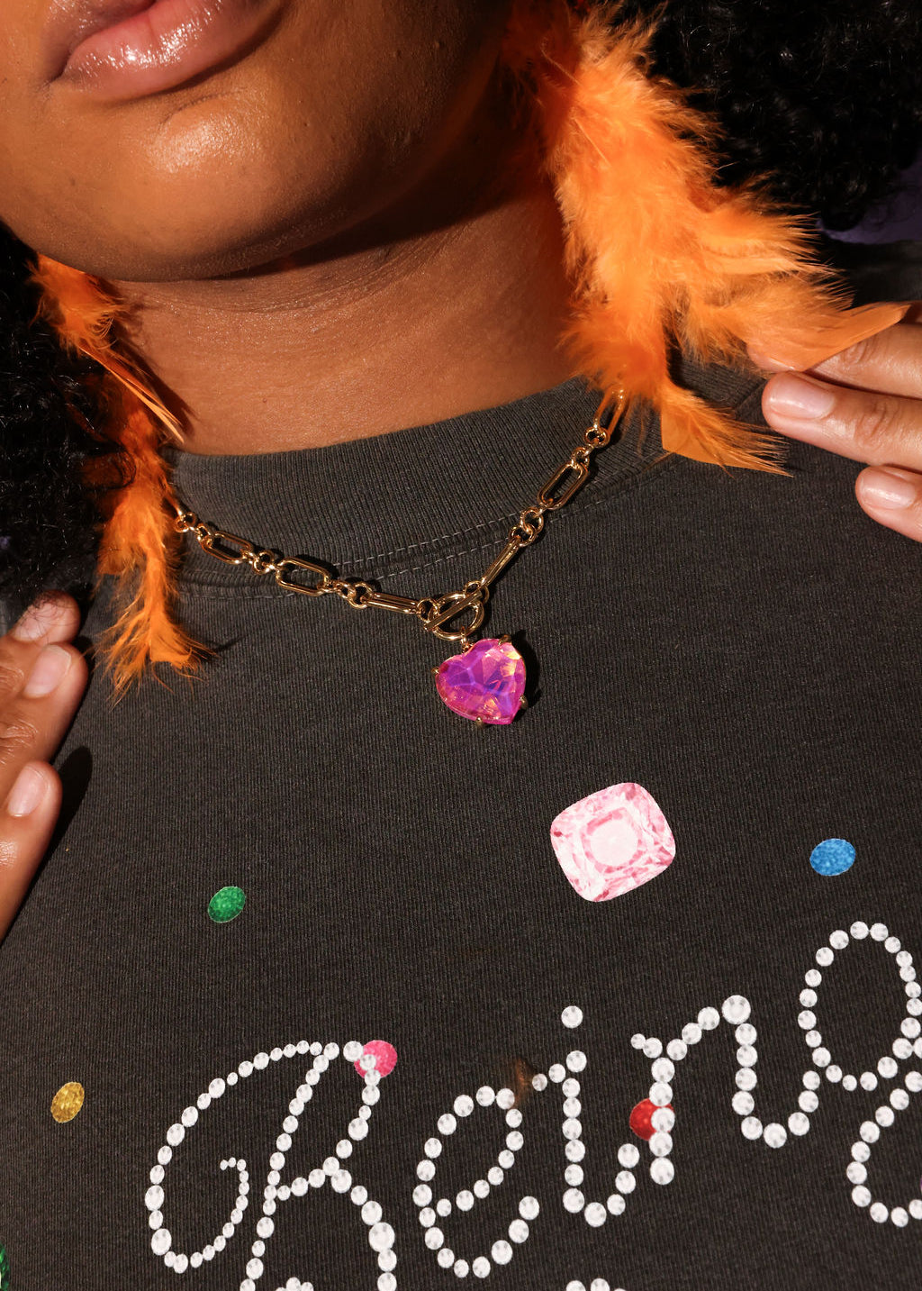 Person wearing a dark shirt with colorful text and beads, holding an orange feathered earring