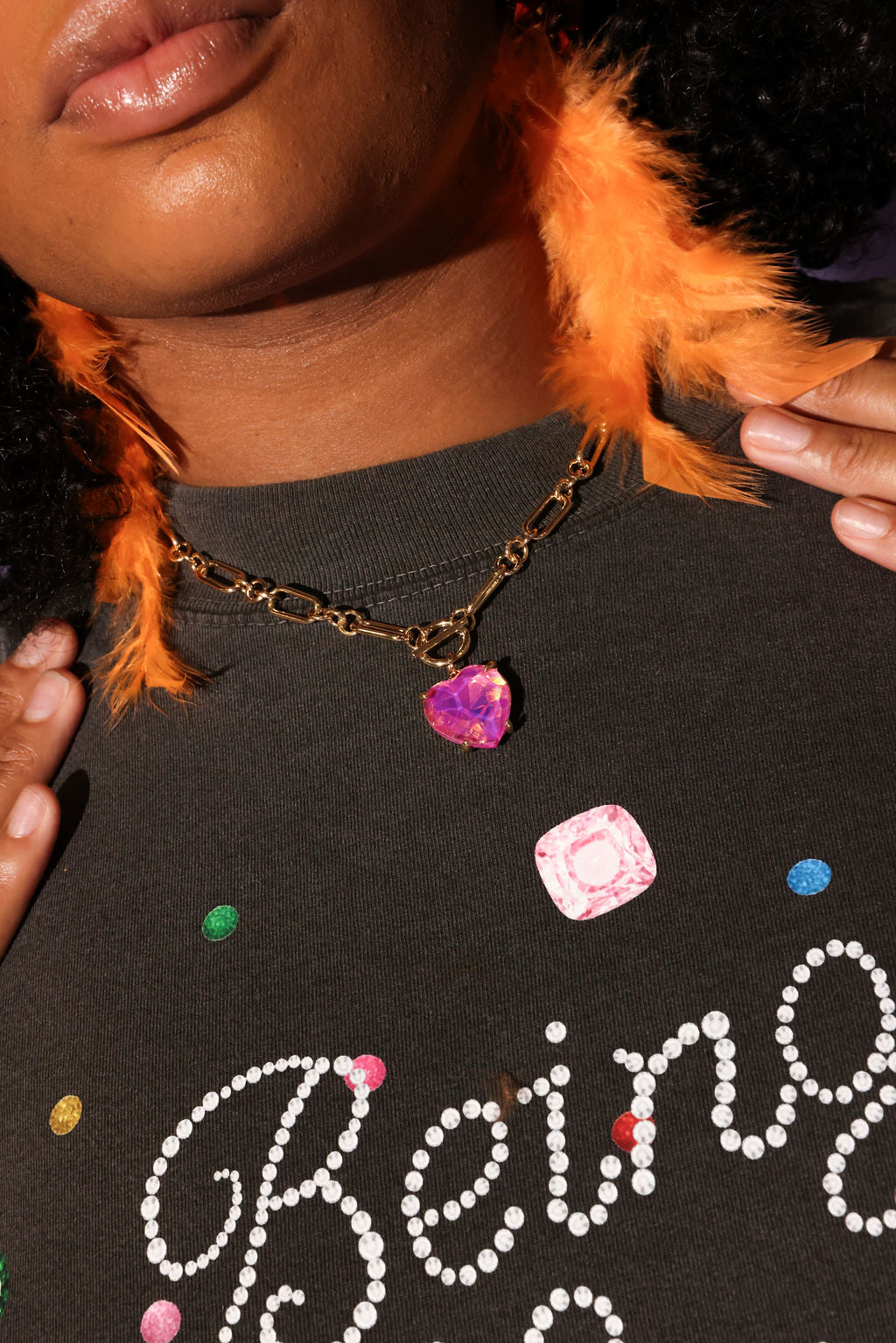 Person wearing a dark shirt with colorful text and beads, holding an orange feathered earring