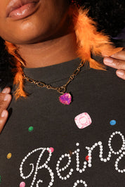 Person wearing a dark shirt with colorful text and beads, holding an orange feathered earring
