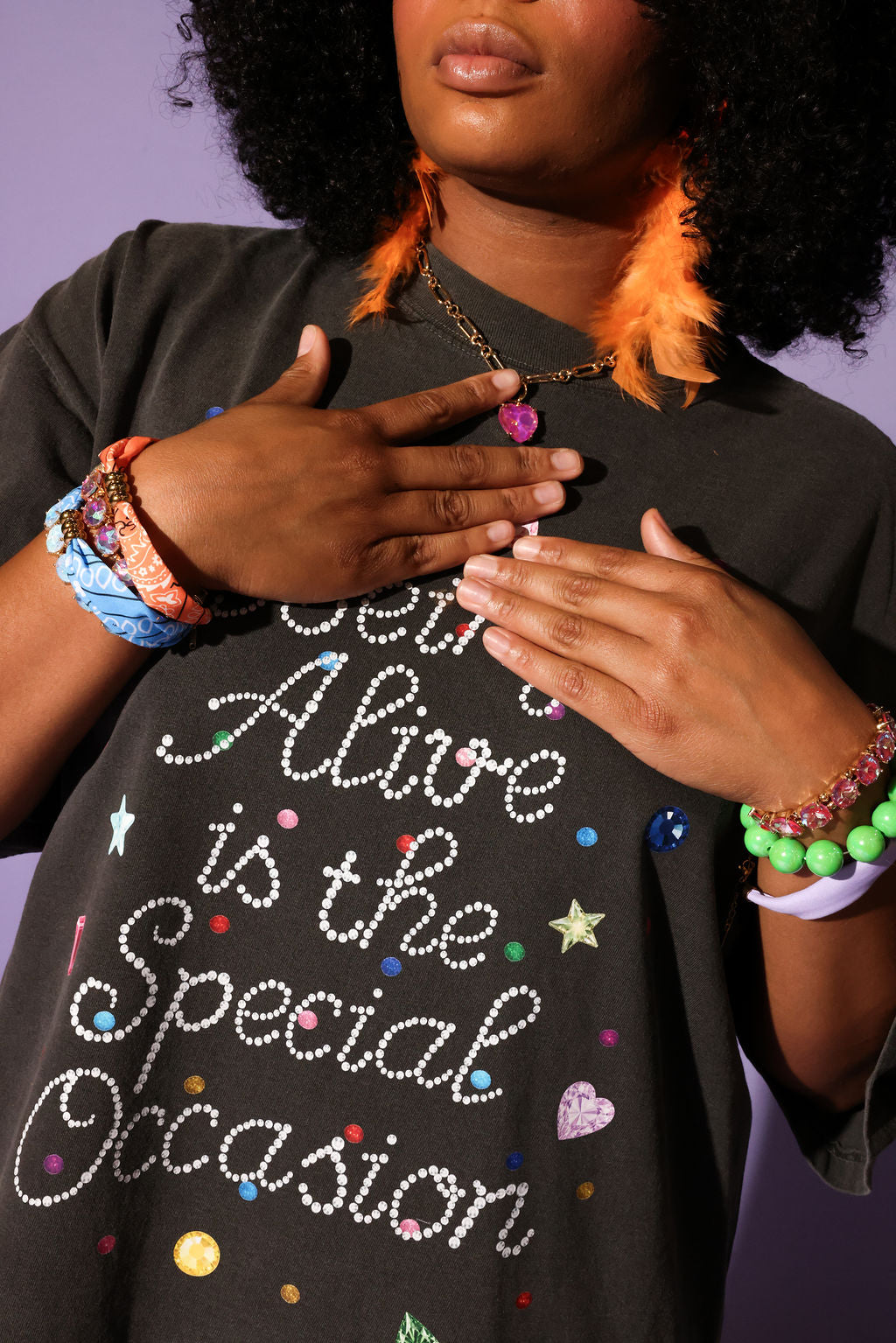 Person wearing a black t-shirt with colorful text and accessories on a purple background