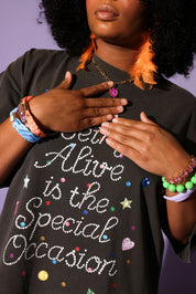 Person wearing a black t-shirt with colorful text and accessories on a purple background