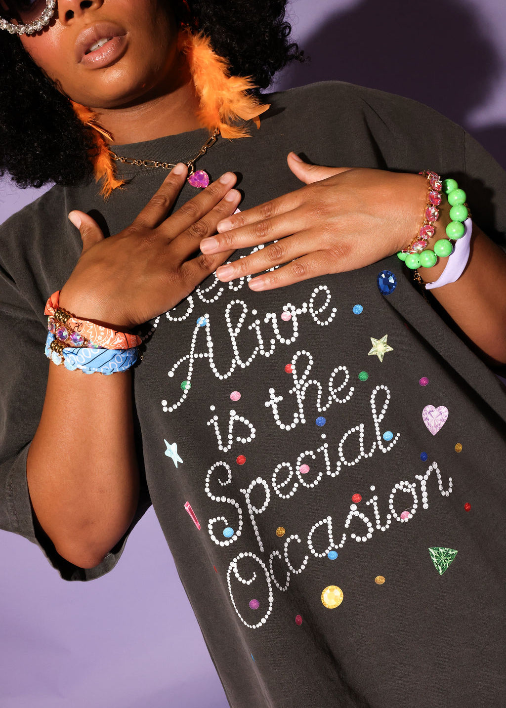 Person wearing a black t-shirt with colorful text and designs, standing against a purple background
