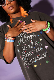 Person wearing a black t-shirt with colorful text and designs, standing against a purple background