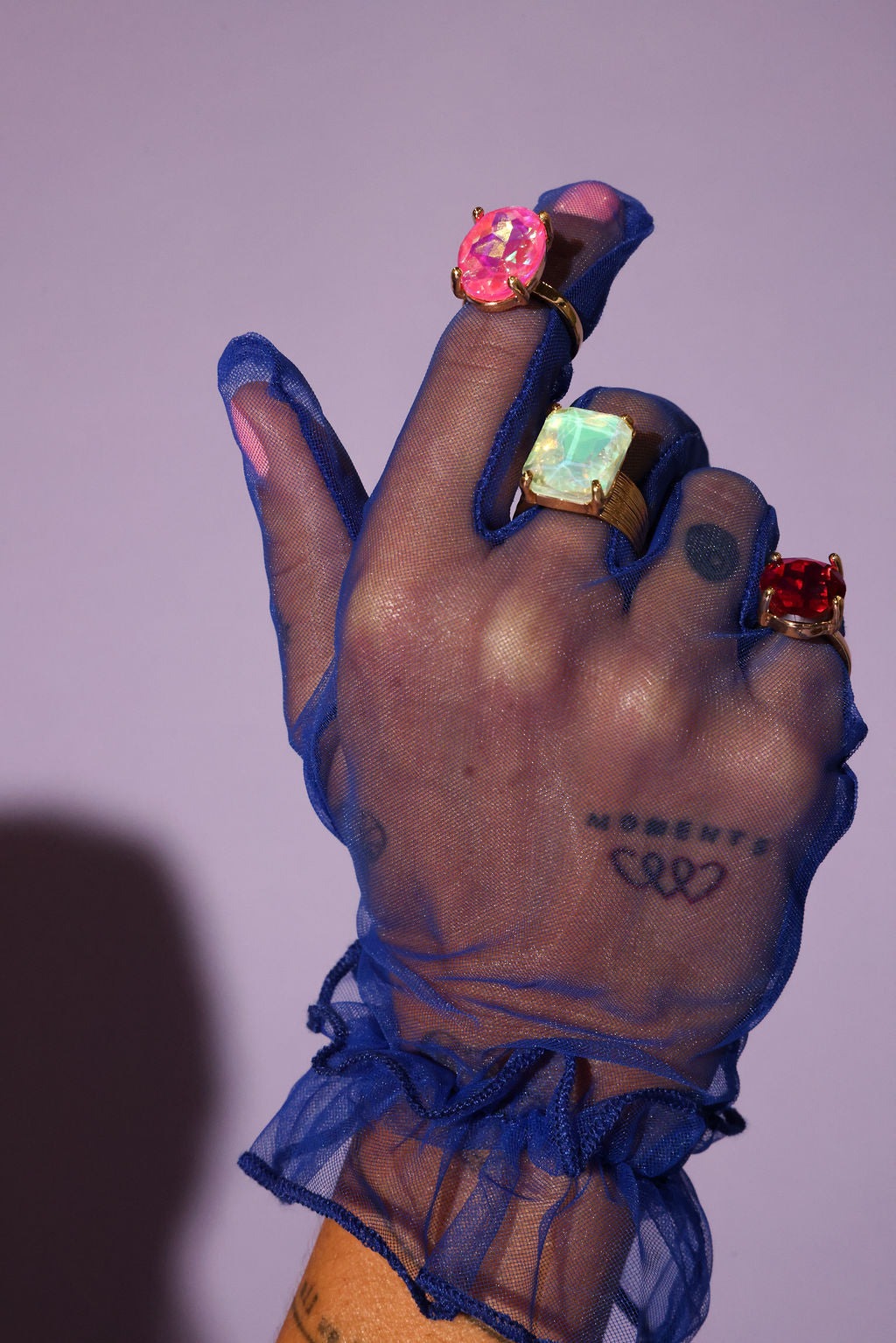 Hand with blue sheer glove and colorful rings on a purple background