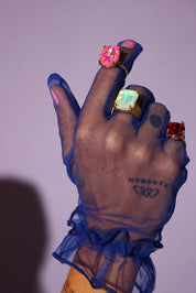 Hand with blue sheer glove and colorful rings on a purple background