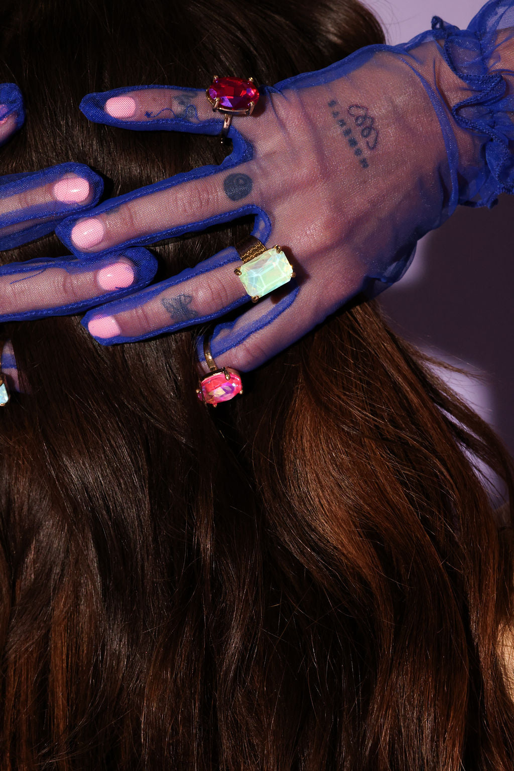 Close-up of hands with blue gloves and colorful rings on a blurred background