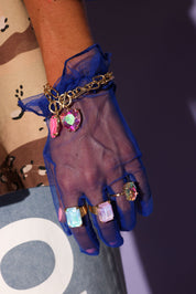 Hand wearing a blue glove with colorful gemstone rings and bracelets
