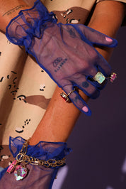 Sheer blue glove with decorative charms on a wrist against a dark background