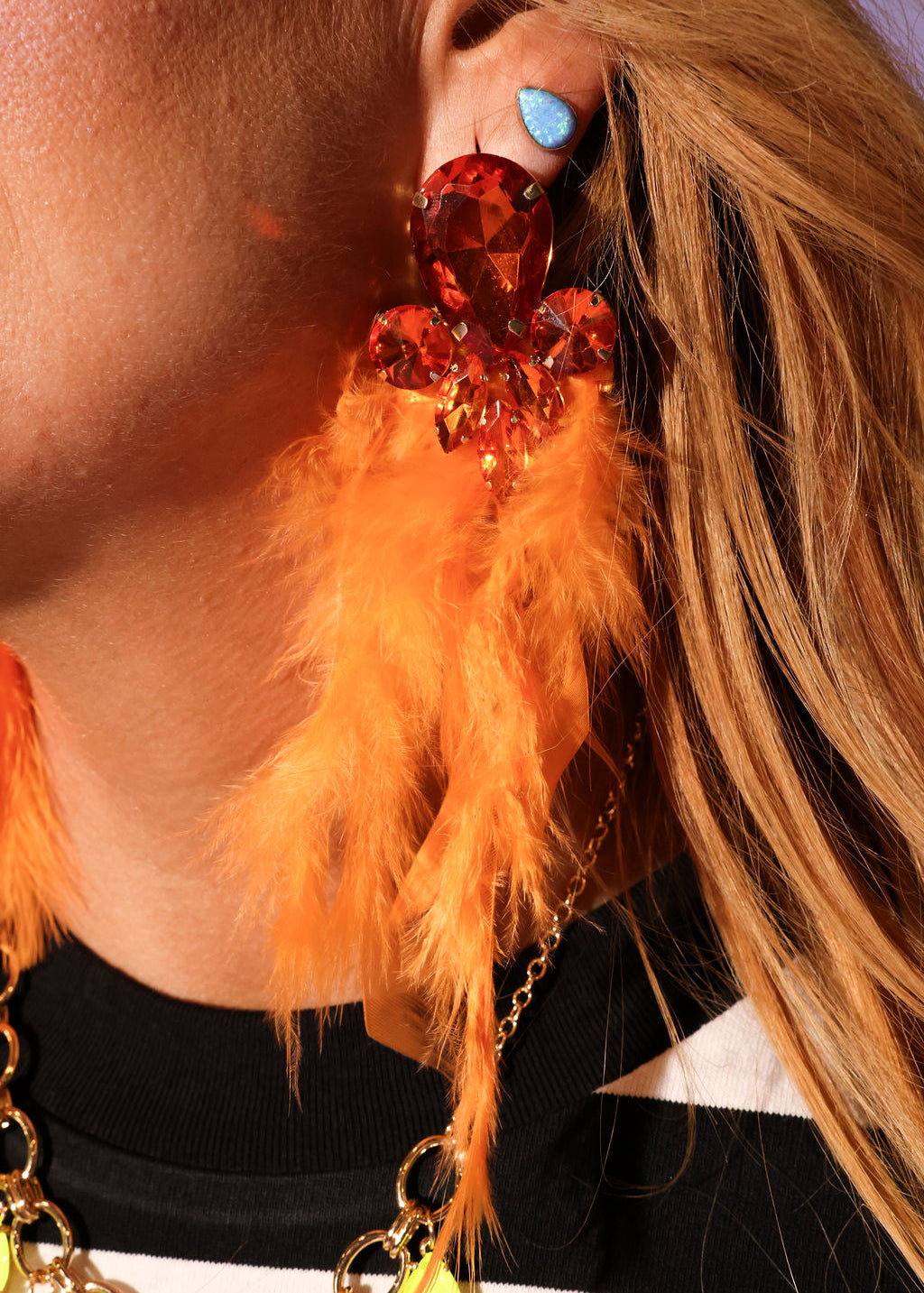 Close-up of a person wearing a feathered earring with orange feathers and a large red gemstone