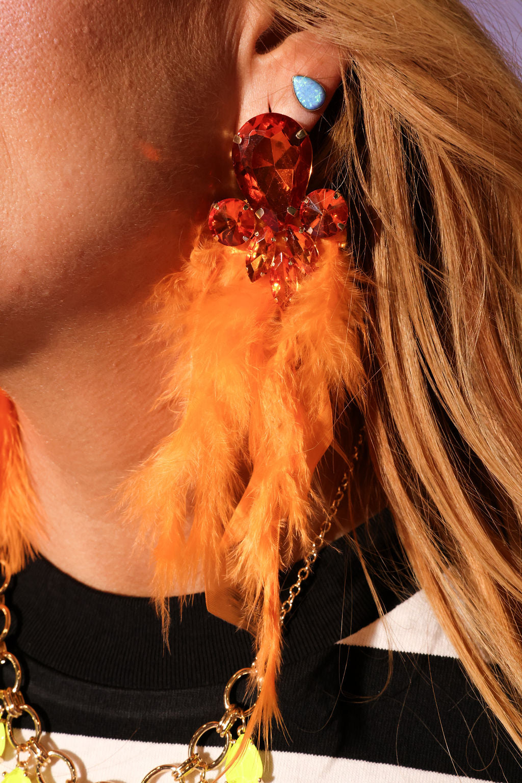 Close-up of a person wearing a feathered earring with orange feathers and a large red gemstone