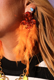 Close-up of a person wearing a feathered earring with orange feathers and a large red gemstone