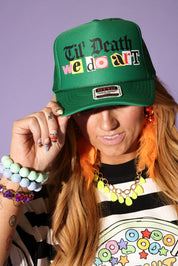 Person wearing a green cap with colorful text and multiple bracelets on a purple background