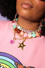 Person wearing a colorful beaded necklace with charms on a pink shirt with a rainbow design