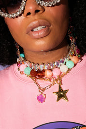 Person wearing a colorful beaded necklace with star charm on a pink background