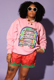 Person wearing a pink sweatshirt with a rainbow design and text, red shorts with green trim, and sunglasses on a purple background