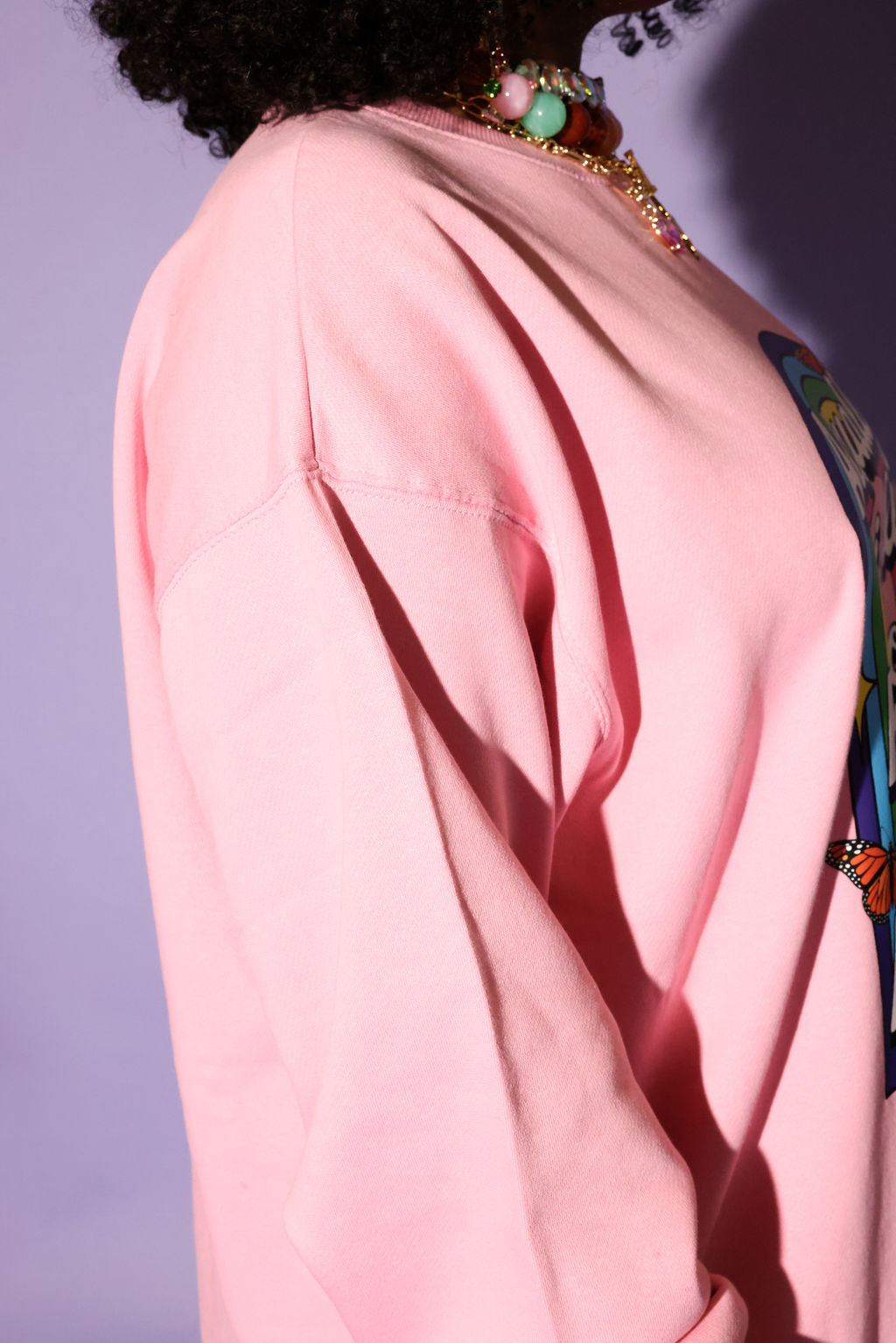 Close-up of a person wearing a pink garment with colorful accessories on a purple background, side view