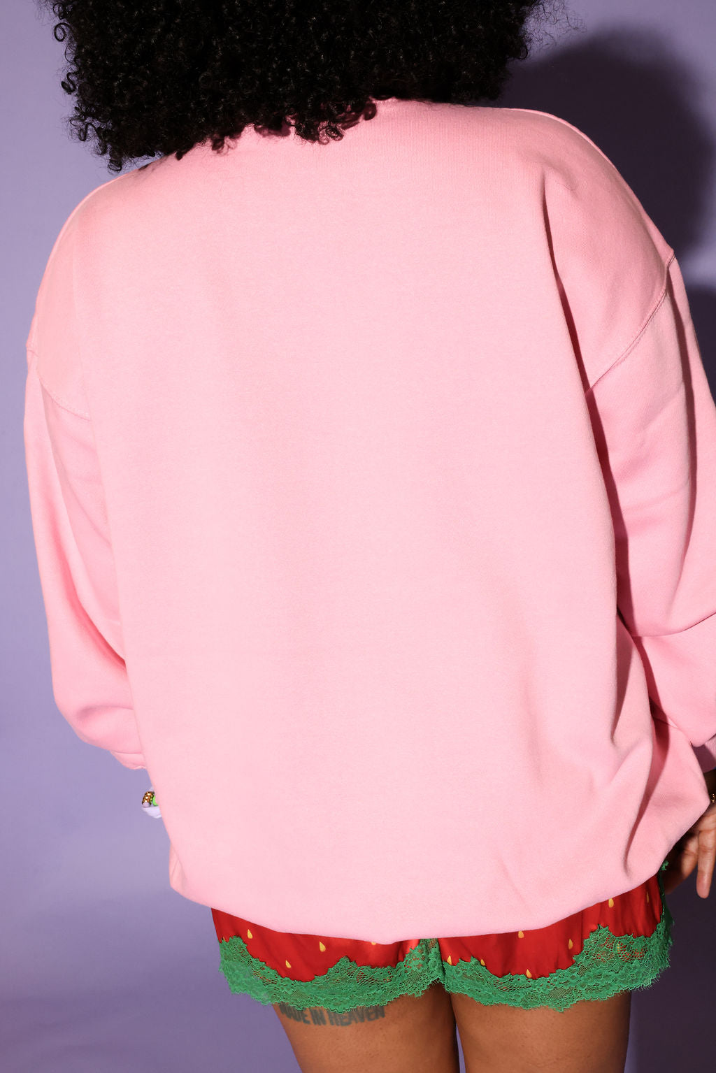 Person wearing a pink jacket and red shorts with green trim against a purple background, back view