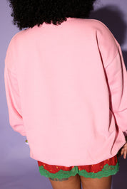 Person wearing a pink jacket and red shorts with green trim against a purple background, back view