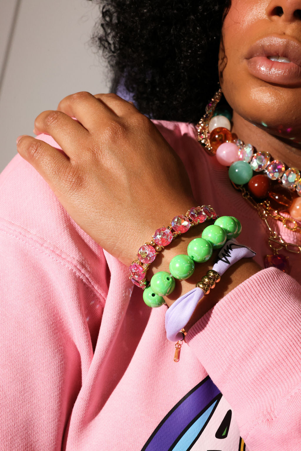 Person wearing colorful beaded bracelets on a pink background