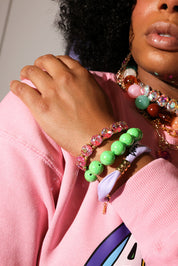 Person wearing colorful beaded bracelets on a pink background