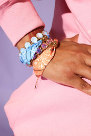 Close-up of a hand wearing colorful bracelets on a pink background