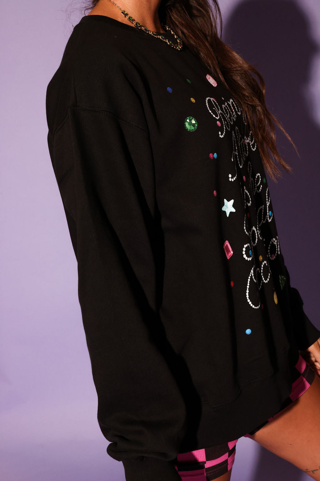 Black sweatshirt with colorful embellishments on a purple background, side view